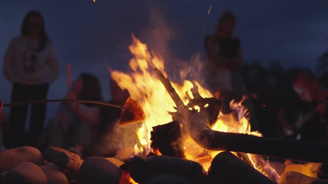People gather around a glowing campfire, toasting marshmallows and bonding in the outdoors. The firelight casts a warm glow, highlighting joyful moments and creating lasting memories