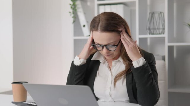 Professional woman in formal attire feeling stressed and frustrated during a busy workday, sitting at her desk with a laptop. Corporate office environment highlights emotional exhaustion and pressure