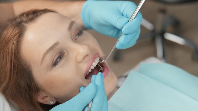 Closeup of female patient receiving routine dental examination, mouth open while dentist uses mirror and probe. Professional oral care and hygiene concept in contemporary medical environment