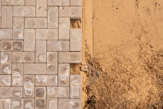 Top-down view of interlocking concrete paver pattern contrasting with prepared sand bed