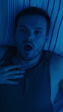 A man suddenly wakes up gasping for air during the night, illustrating symptoms of sleep apnea and interrupted breathing during sleep. Concept of sleep disorders, respiratory health, and nighttime bre