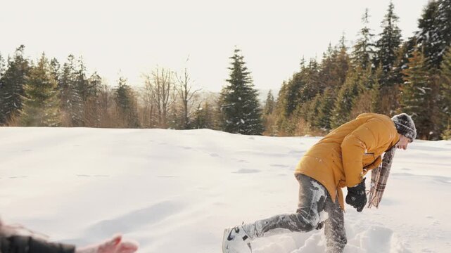 A cheerful young man enjoys a playful moment in a snowy forest, dressed warmly in a yellow coat and scarf. The serene winter scene captures the essence of outdoor fun and seasonal adventure