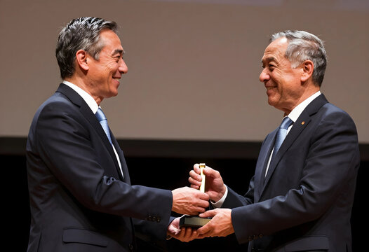 Two smiling senior men in suits exchanging a golden award trophy during a formal ceremony event, the men are seen in profile, facing each other with happy expressions