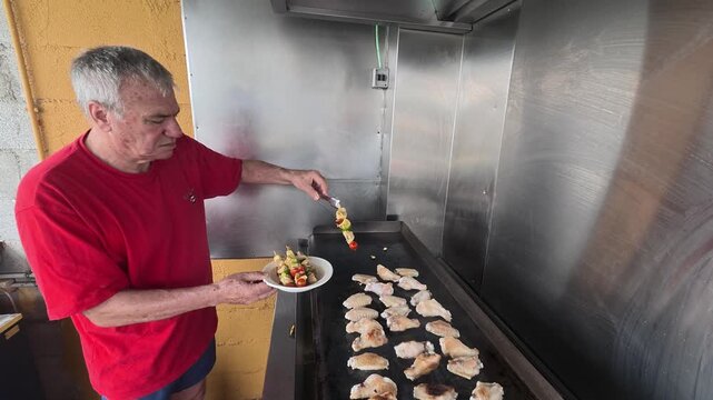 Senior man grilling chicken wings and skewers on commercial griddle