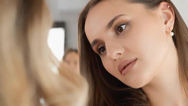 A beautiful young woman with smooth complexion and subtle makeup gazes intently at someone in a serene indoor setting. The image captures a moment of connection and gentle focus