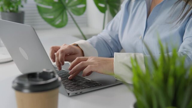 Closeup of female hands typing on a laptop keyboard in a stylish workspace with natural light and greenery. Remote work and digital communication are essential for modern business efficiency
