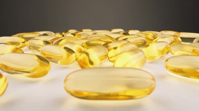 A collection of translucent yellow softgel capsules is displayed in a scattered arrangement on a smooth white background. The image highlights modern health trends and dietary supplement usage