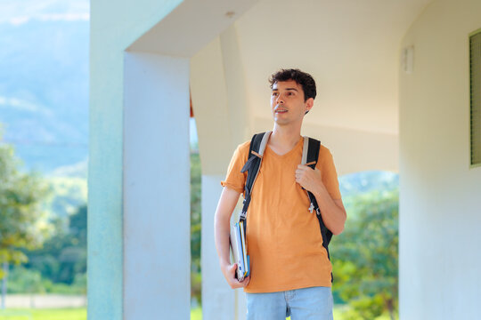 Young university student carrying books and a backpack while walking across campus. Concept of higher education, academic life, learning, and student routine.