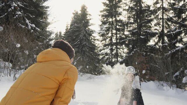 Two people enjoy a playful snowball fight in a snowy forest, dressed warmly in winter clothing. The sunlight creates a magical atmosphere, highlighting the fun and excitement