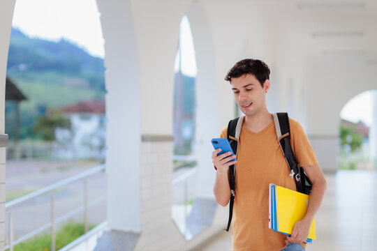 Young university student using a smartphone while walking on campus. Concept of higher education, digital learning, mobile technology, and student life.