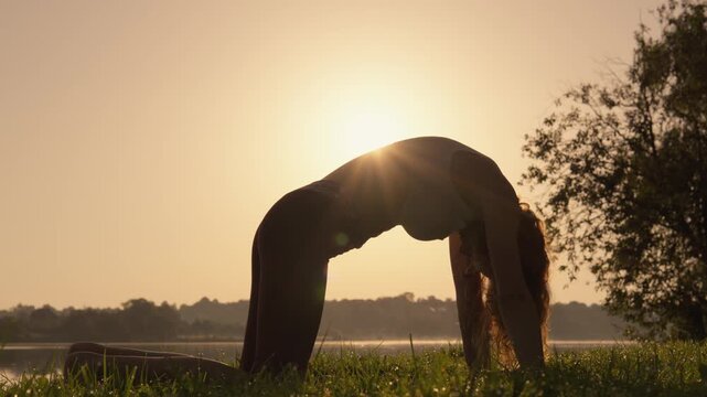 Young woman in sportswear does yoga in the early morning, stretching in upward facing dog pose on a grassy field. The golden sunrise creates a tranquil and inspiring outdoor setting