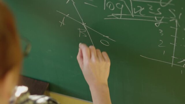 Close up view of a student or teacher solving math problems on a chalkboard, with visible formulas and diagrams. The scene captures a moment of active learning and academic engagement
