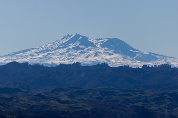 Fototapeta premium The majestic snow-capped peaks of Mount Ruapehu rise above the rolling green hills of the Ruapehu District in New Zealand's North Island.