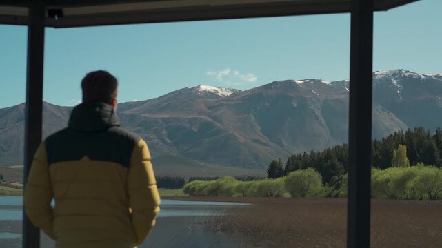 Man in a yellow jacket standing on a wooden pier looking towards the mountains at Laguna La Zeta, Esquel, Chubut, Argentina.