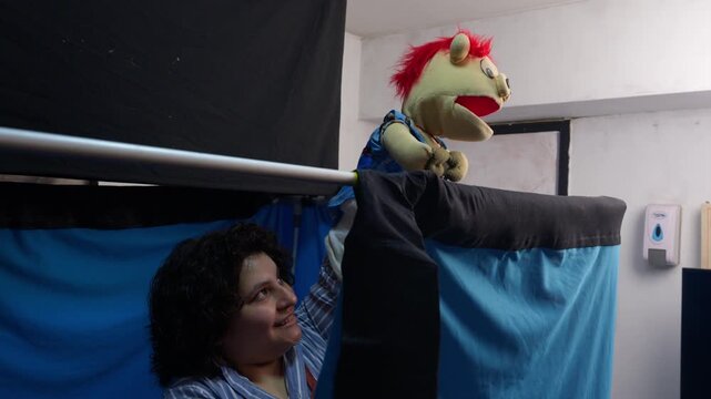 Female puppeteer performing a puppet show from behind a blue curtain