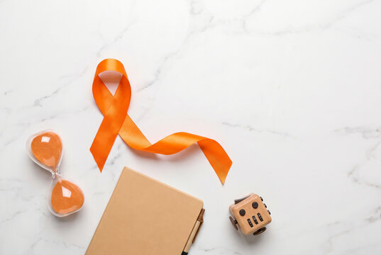 Orange awareness ribbon arranged on a clean white marble surface
