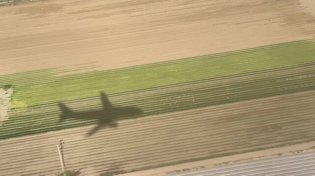 Aerial view of an airplane shadow gliding across green golf courses, agricultural fields, and rural landscapes during landing approach, showcasing travel, flight, and nature from above