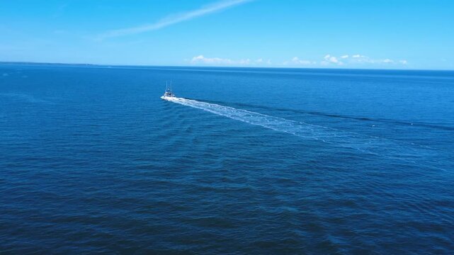 A fishing vessel sails away on the St. Lawrence River, leaving a crisp wake trail across the smooth blue water.