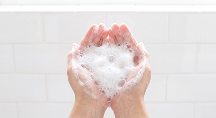 Fototapeta premium Close-up commercial photograph of cupped hands holding rich white soap lather and bubbles, minimalist bright bathroom setting, white tile background, clean airy high-key lighting, high resolution.