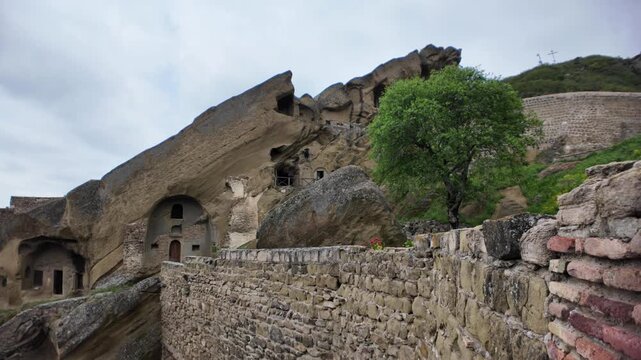 Woman on ancient rock steps, enjoying the panoramic view of the historic David Gareji rock-hewn monastery complex nestled in the green valley landscape of Georgia's Middle Ages heritage site