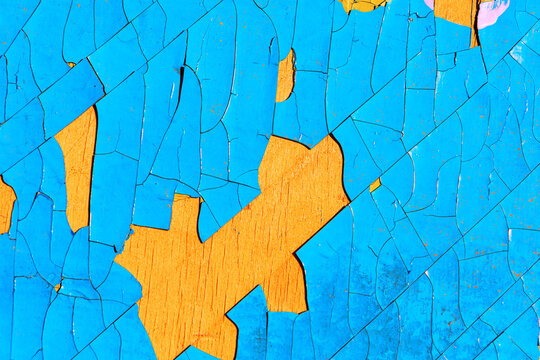 Weathered surface shows vivid peeling paint, where cracked layers of blue reveal bold orange underneath in a striking abstract pattern
