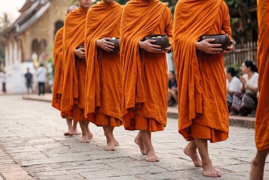 Line of traditional buddhist monks walking barefoot in orange robes carrying black alms bowls