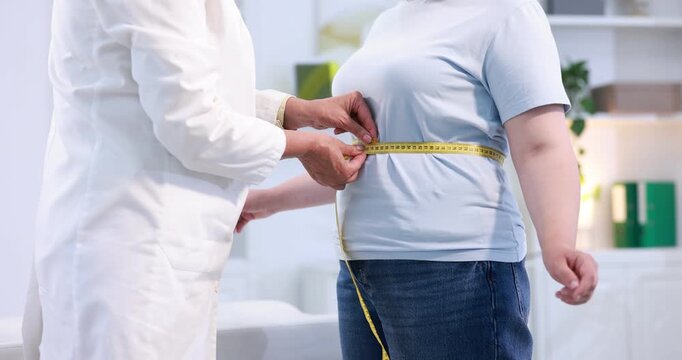 Weight loss. Nutritionist measuring overweight woman's waist and hips with tape in clinic, closeup
