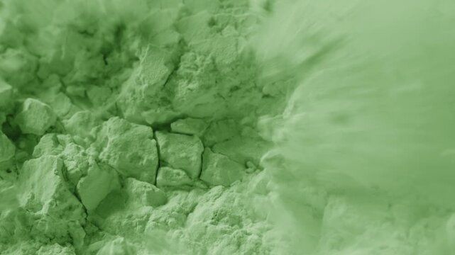 Macro slow-motion footage of broken into pieces pale green powder surface being blown with air stream, breaking its structure and chipping it into small pieces