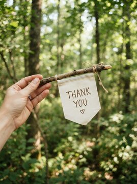Hand holding a thank you banner in a forest setting.
