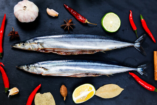 Raw saury fish surrounded by chili garlic lime star anise dark slate