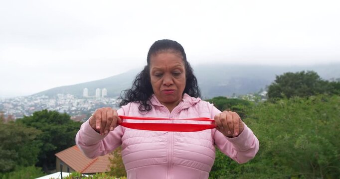 Senior African-American woman gripping red band, pulling then releasing for fitness on terrace