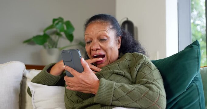 Senior African American woman in green knit seeing text holding phone gasping on couch
