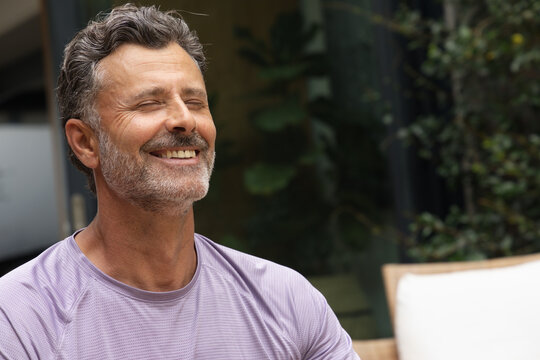 Middle-aged man smiling with eyes closed, sitting on patio chair wearing purple athletic shirt