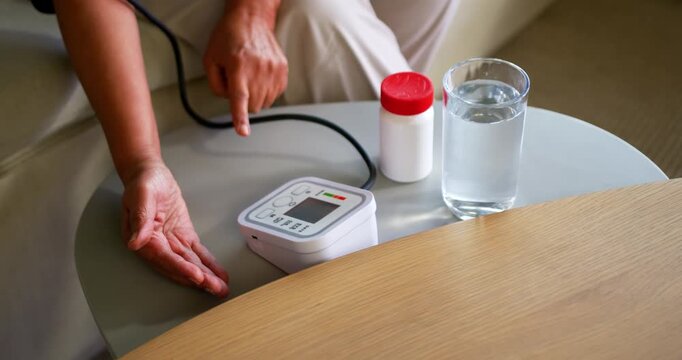 African American senior pressing BP buttons at side table with cuff on, testing, pill bottle, water