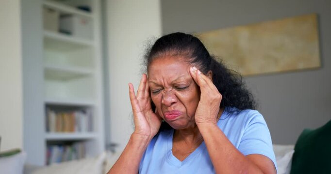 Senior African American woman pressing temples, trying to ease sudden headache while seated on sofa