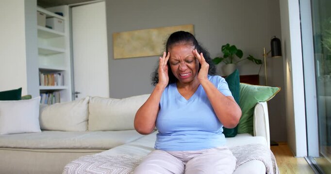 African American senior woman pressing temples and pursing lips to ease headache living room sofa