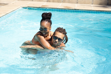 Fototapeta premium African American couple playing in backyard pool, wearing sunglasses and swimwear, near tiled deck