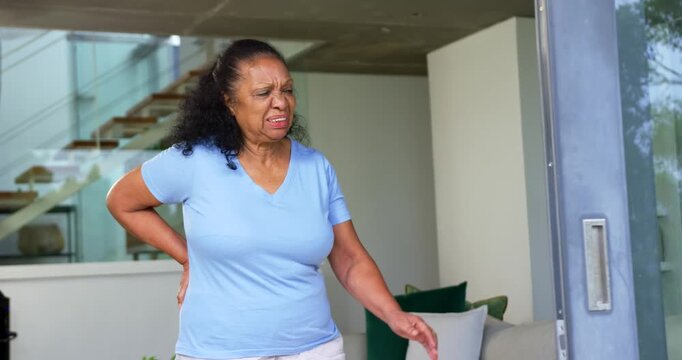 Senior African American woman wincing from back pain, leaning on sliding door at home, steadying