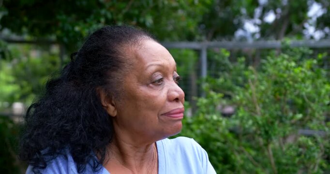 Senior African woman on garden bench in blue top turning head as camera widens, meeting gaze