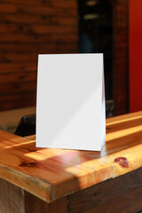 Fototapeta premium Blank table tent menu mockup on a rustic wooden table in a cozy restaurant or café interior. Vertical folded card display with copy space, ideal for menu design, branding, promotional offers
