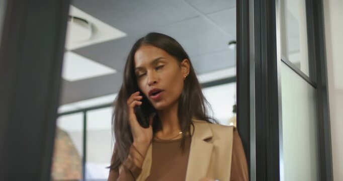 Taking work call, adult woman in blazer at office speaking on phone gesturing leaning by partition