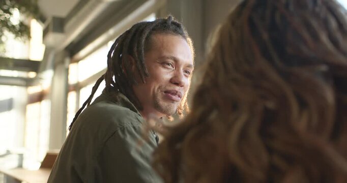African American couple chatting at cafe after greeting man leaning laughing pausing by big windows
