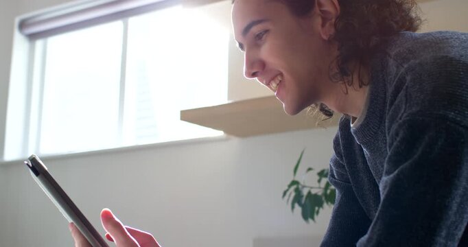 African American man sitting at home by window holding tablet tapping and smiling reading content