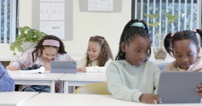 African American child girls sharing tablet after teacher cue, leaning in tapping screen in class