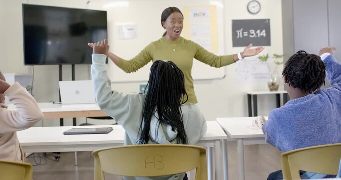 African American female teacher in class gesturing stepping to call pupil to answer at ?