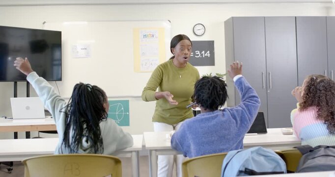 African American teacher with tablet asking pointing to ? poster in class teen girls raising hands