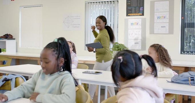 African American woman teacher raising hand holding tablet teaching math kids watching and writing