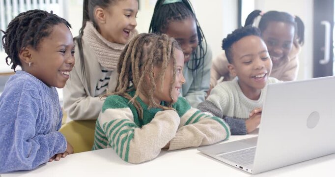African American preteens gathering around silver laptop on table operator typing reacting to clip