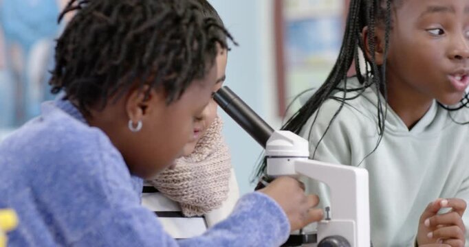 Diverse female children helping green-sweatshirt girl turning slide on microscope, examining sample