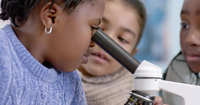 Diverse teen girls examining microscope in school lab curiosity guiding girl in blue peering lens